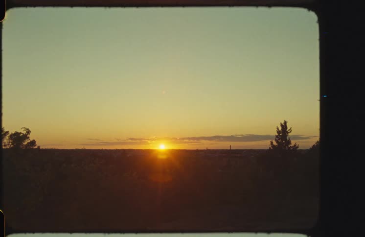 A golden sunset over a distant city skyline and silhouetted forest, captured on vintage Super 8mm film