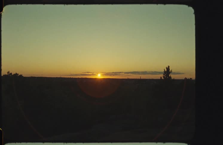 Authentic Super 8 film captures a beautiful sunrise with a warm lens flare over a silhouetted landscape