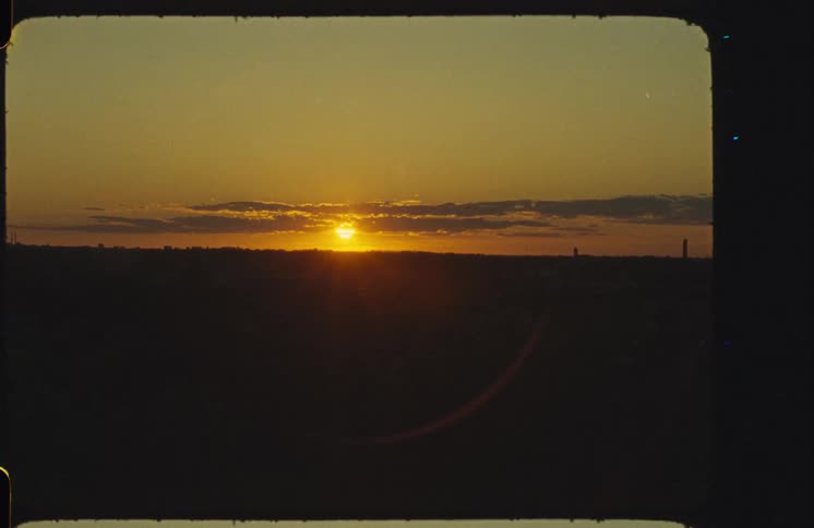 A static shot of a golden sunset over a silhouetted horizon, captured on Super 8mm film