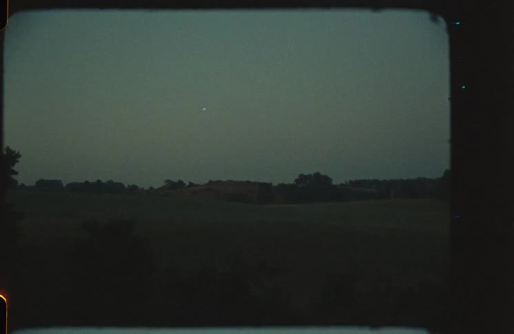 Vintage 8mm film shows a grainy, dark rural landscape with authentic dust, scratches, and dramatic light leaks