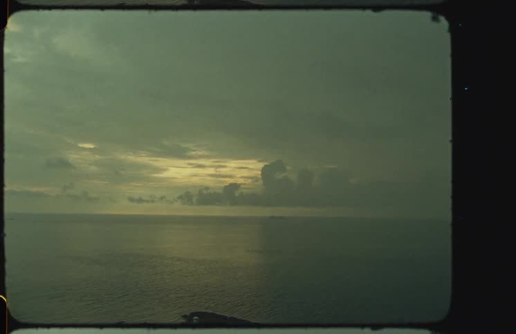 A vintage Super 8mm shot of a moody, overcast sunset over a calm ocean horizon