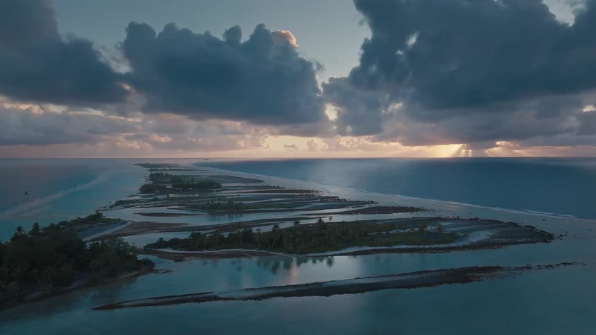 Stunning aerial view of a tropical atoll as the sun sets behind dramatic clouds over the turquoise ocean