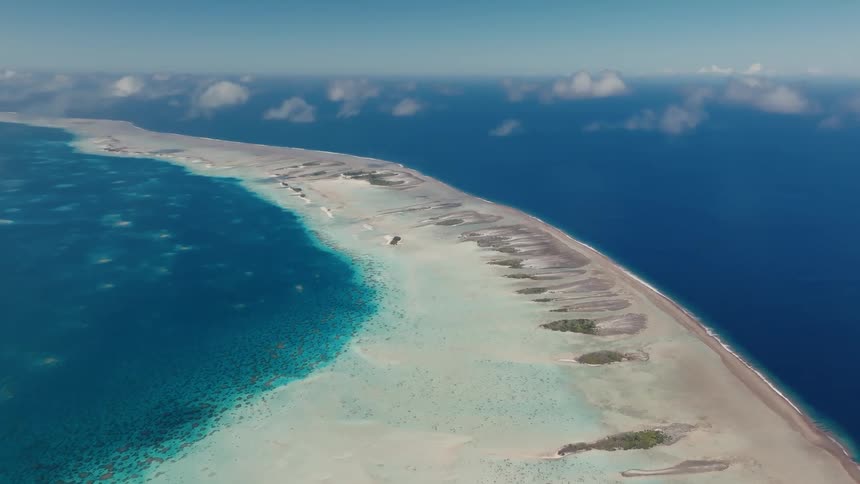 A stunning high-angle aerial view of a long tropical atoll separating a shallow turquoise lagoon from the deep blue ocean