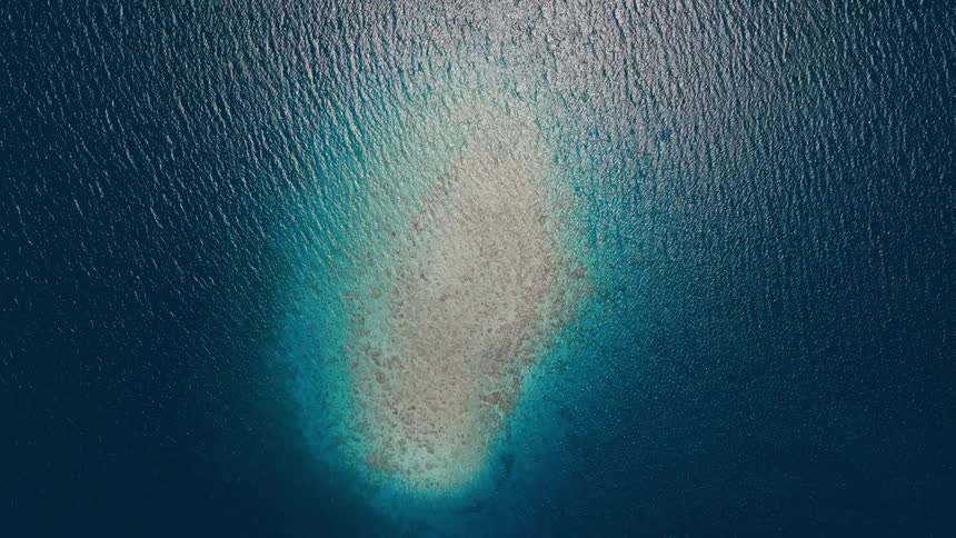 Top-down aerial view of a beautiful coral atoll in the middle of the deep blue ocean