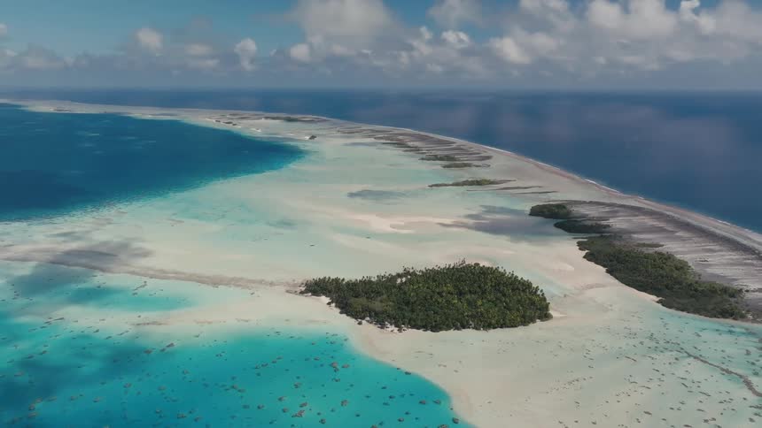 A breathtaking aerial view of a tropical atoll in French Polynesia, featuring a lush green island surrounded by a vibrant turquoise lagoon