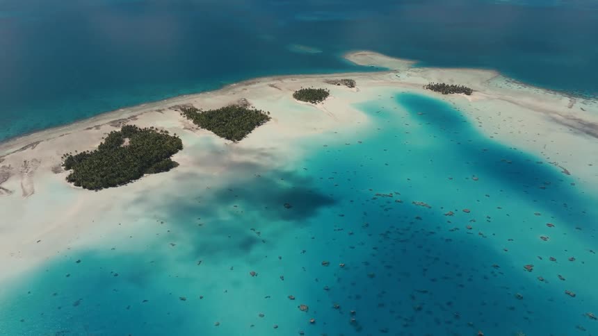 A stunning high-angle aerial view captures a beautiful tropical atoll with lush green islands nestled in a shallow, turquoise lagoon