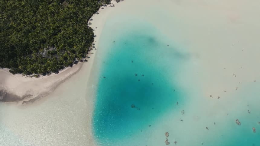 Ascending aerial shot over a breathtaking tropical paradise with crystal clear turquoise water, coral reefs, and a lush green island
