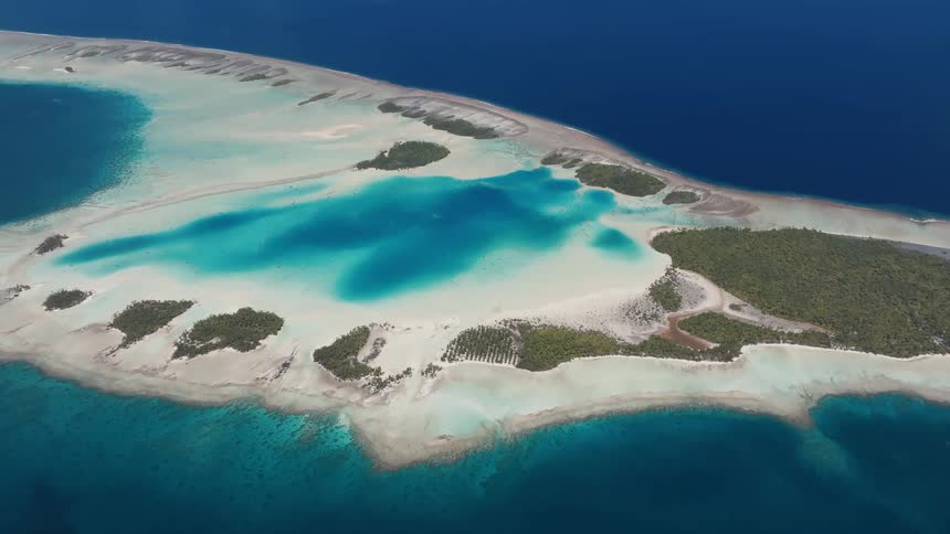 Stunning high-angle aerial view of a pristine tropical atoll with turquoise lagoons, white sandbars, and lush green motus surrounded by the deep blue ocean