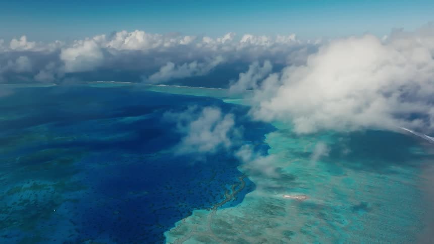 A breathtaking aerial perspective captures the vibrant blue and turquoise hues of a tropical ocean, revealing coral reefs beneath a sky of fluffy white clouds