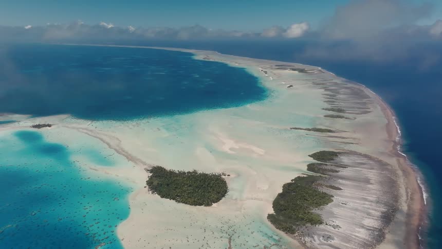 Stunning high-altitude aerial view of a beautiful tropical atoll with turquoise lagoons, white sand, and lush green islands surrounded by the vast blue ocean