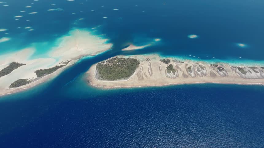 Stunning high-angle aerial view of a vibrant turquoise and blue tropical atoll surrounded by the vast ocean