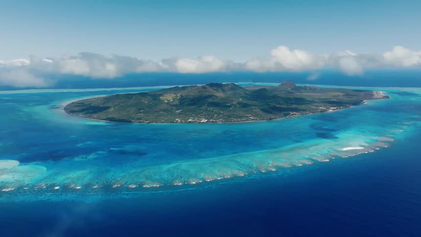 Cinemagraph of an idyllic tropical island with lush green mountains, a turquoise coral reef lagoon, and a blue sky with clouds