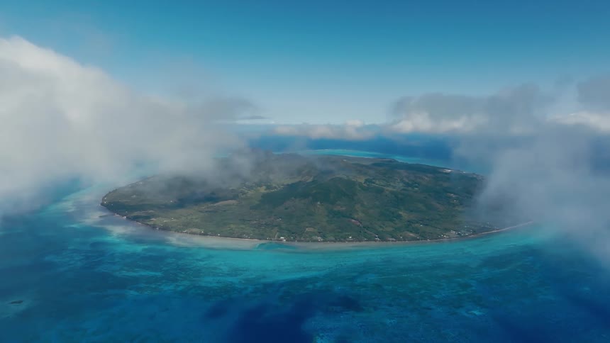 A majestic aerial view shows a lush tropical island paradise peeking through a frame of soft white clouds over a vibrant turquoise ocean