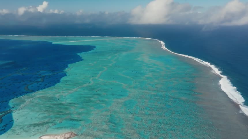 An expansive aerial view showcases the brilliant turquoise waters of a tropical lagoon contrasting with the deep blue of the open ocean