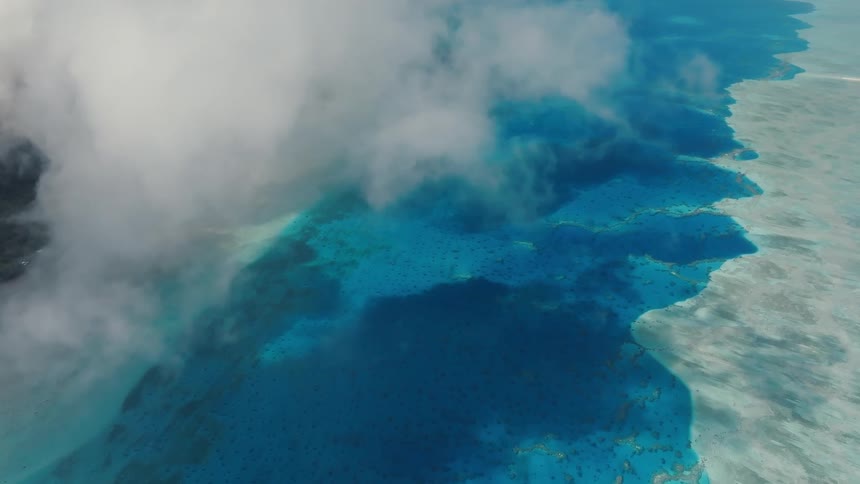 A serene aerial view from above the clouds reveals the stunning turquoise waters and coral reefs of a tropical ocean paradise