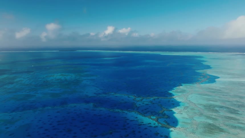 A stunning high-altitude aerial view of the deep blue ocean meeting the turquoise waters of a tropical coral reef