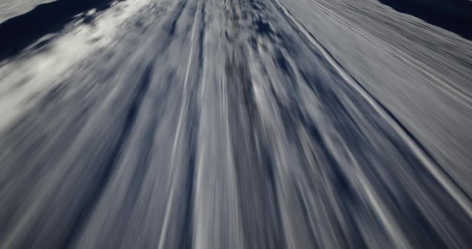 A low-angle, abstract, fast-moving perspective of a road surface with passing shadows