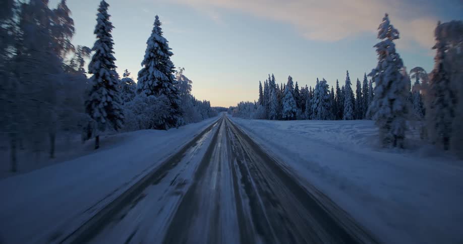 A point-of-view drive along a slippery, icy road through a beautiful snow-covered forest during a winter sunrise