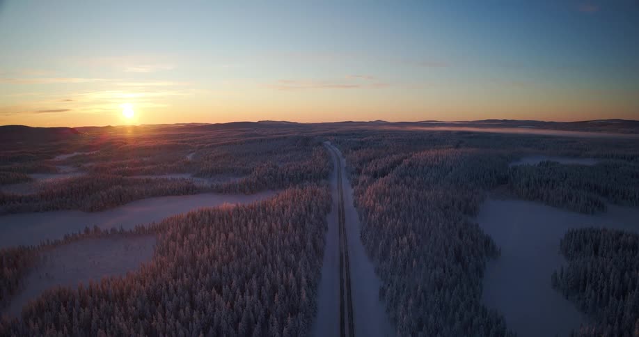 Stunning aerial footage captures an empty highway running through a vast, frozen forest wilderness at sunset in winter