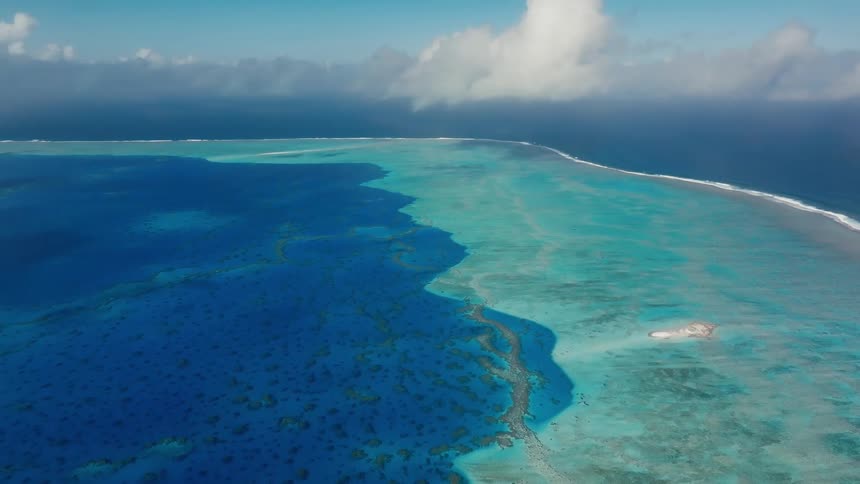 A majestic aerial still shot captures the vibrant colors of a coral reef separating the deep blue ocean from the turquoise lagoon
