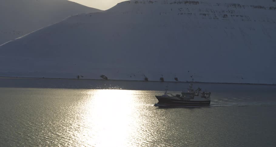 A fishing trawler sails through a sunlit arctic fjord, its silhouette stark against the shimmering water and snowy mountains