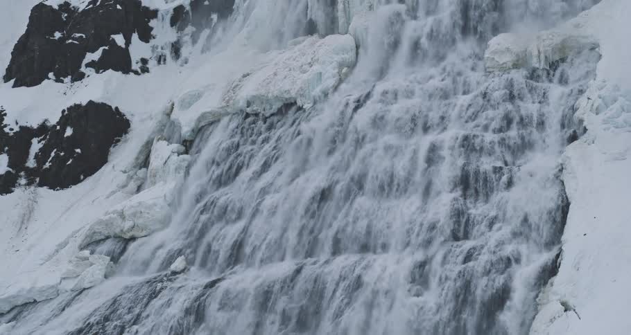 A powerful waterfall crashes down a snow-covered mountain slope in a dramatic winter landscape