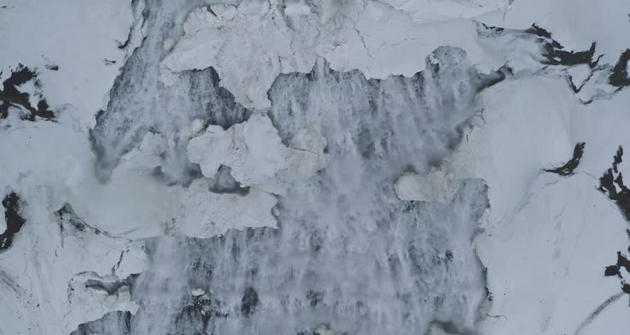 Static top-down aerial view of a powerful icy waterfall cascading through a snowy landscape