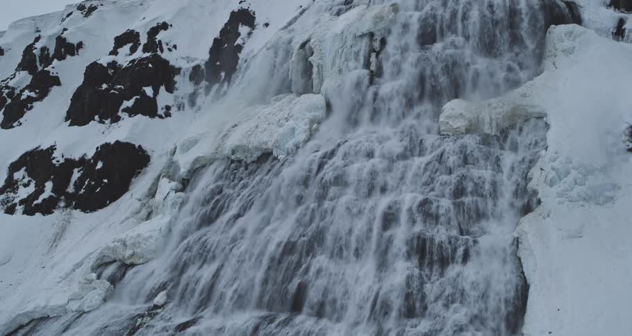 Slow zoom towards a majestic, powerful waterfall cascading down a snow-covered, icy mountain