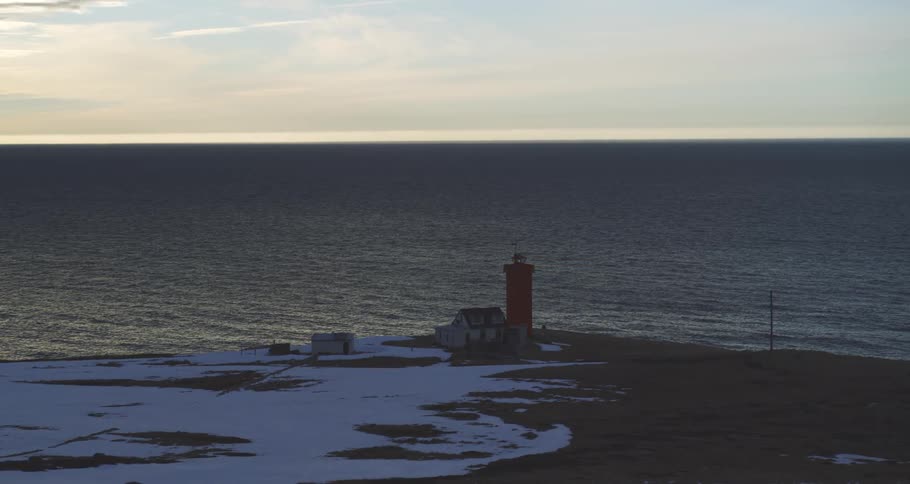 A tranquil timelapse captures the fading light of dusk over a striking red lighthouse on a snowy, remote coastline
