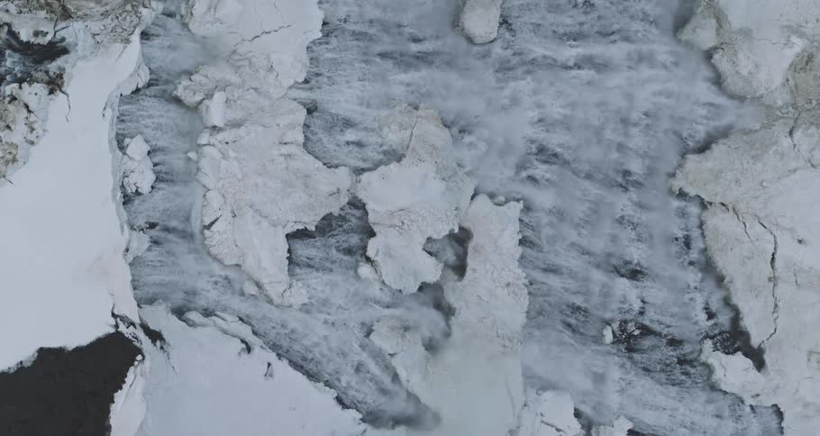 A static overhead view shows a powerful stream of meltwater cutting through a frozen, snowy landscape