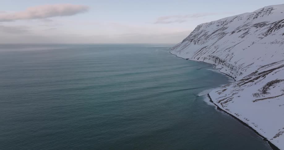 An expansive aerial view of gentle ocean waves rolling ashore along a majestic, snow-covered coastline
