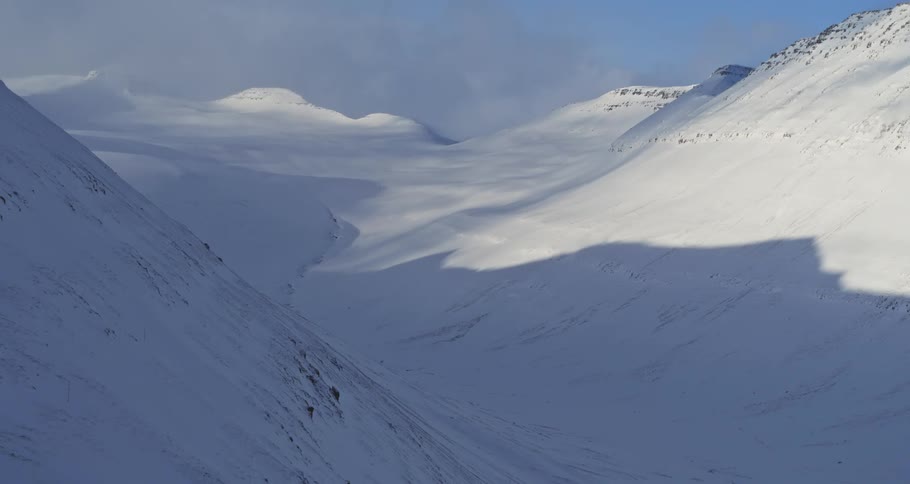 A breathtaking aerial view pulling back to reveal a vast, pristine snow-covered mountain valley under a clear blue sky