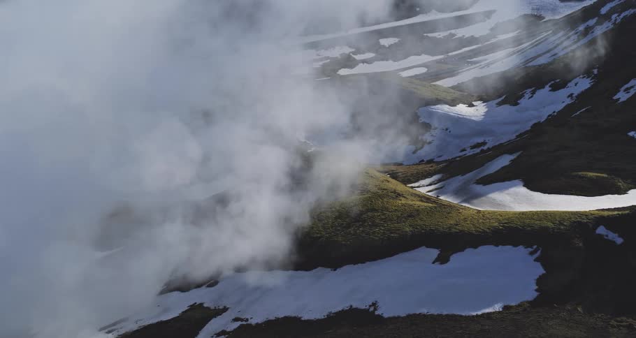 Geothermal steam rises from a snowy mountainside landscape on a sunny day