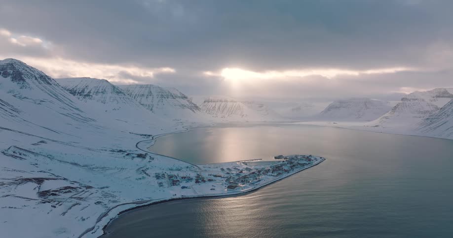 Serene cinemagraph captures a snowy Icelandic fjord village as sunlight pierces through dramatic winter clouds
