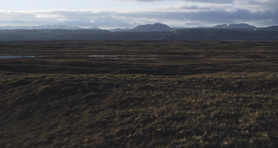 A cinematic aerial shot glides low over a vast, mossy tundra with distant snow-capped mountains on the horizon