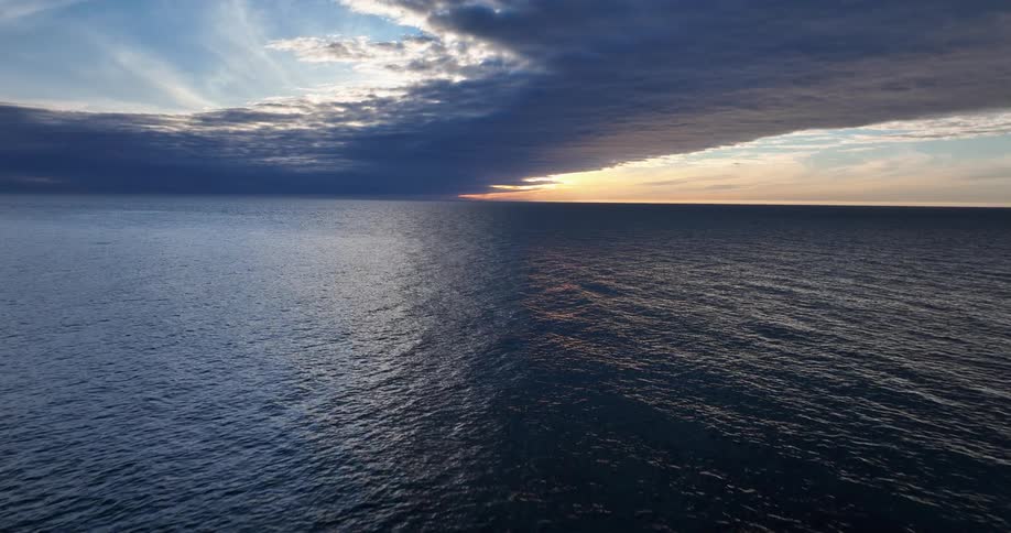A dramatic sunset over the ocean creates a stunning divide between light and shadow as a heavy cloud bank looms overhead