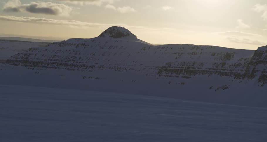 A serene timelapse captures shadows moving across a vast, snow-covered mountain valley at sunrise