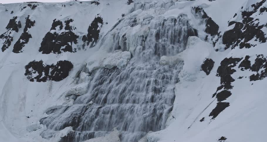 A slow zoom-out reveals the majestic Dynjandi waterfall cascading down a snowy, ice-covered mountain in the Westfjords of Iceland