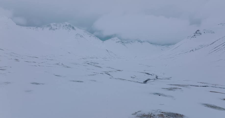 An epic aerial view shows two tiny explorers trekking through a vast, snow-covered mountain valley