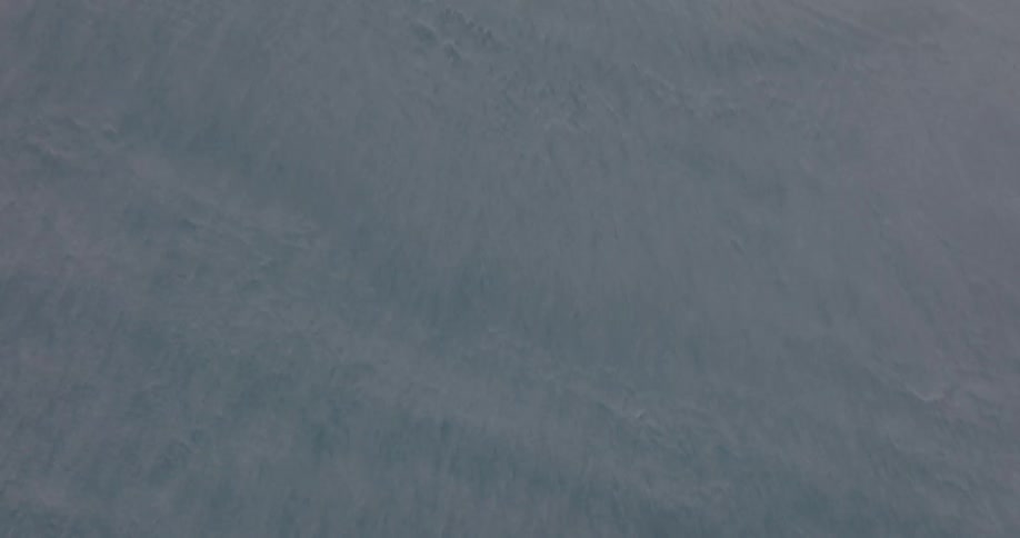 A high-angle aerial shot slowly pulls back to reveal the vast, textured surface of a frozen body of water