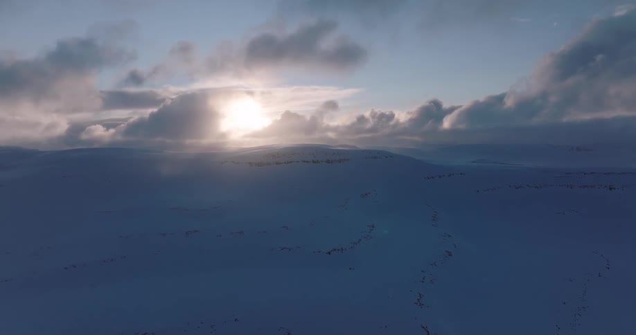 A serene and expansive aerial view shows the sun setting over a pristine, snow-covered arctic tundra