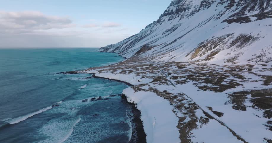 A stationary aerial view captures the dramatic beauty of a snow-covered coastline where mountains meet the turquoise sea