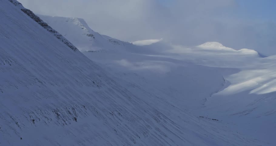 A static wide shot of a vast, desolate, snow-covered mountain valley landscape