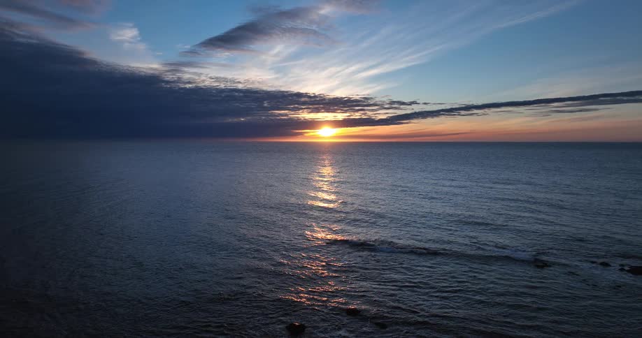 A serene sunset casts a golden reflection across the calm ocean waves under a beautiful, cloudy sky