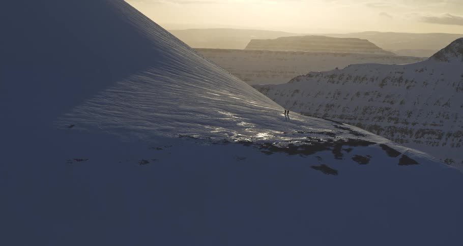 Two adventurous hikers walk along a snowy mountain ridge against a breathtaking sunset backdrop