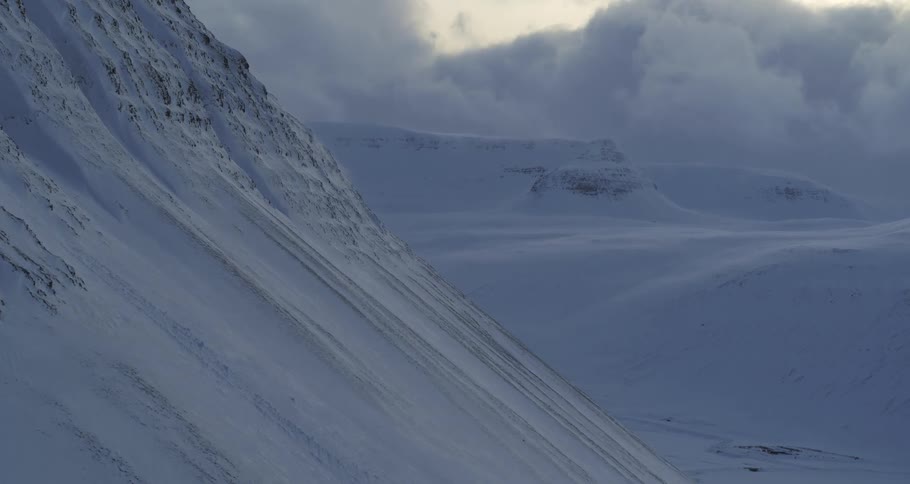 A vast, frozen landscape shows snow-covered mountains under a cloudy sky