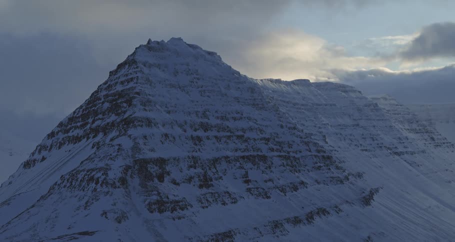 A majestic, snow-covered mountain peak is silhouetted against a dramatic and cloudy sky