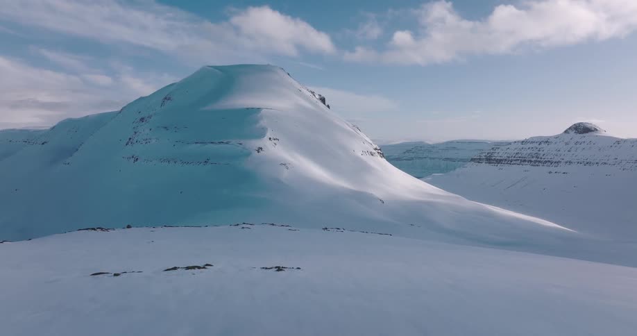 Slow aerial pullback reveals a vast and majestic winter landscape of snow-covered mountains