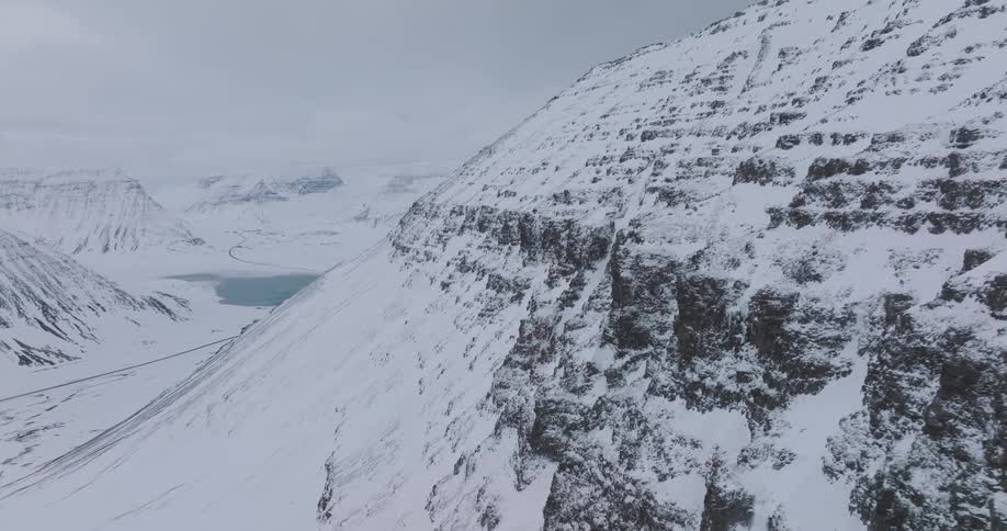 An aerial shot slowly pulls back from a rugged, snow-covered mountainside, revealing a vast and epic winter landscape