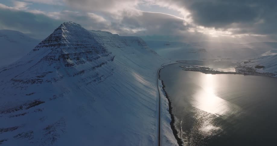 A stunning aerial view of a sunlit fjord next to a vast snow-covered mountain range in Iceland during winter